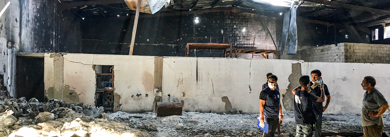 Men stand in a destroyed building in Tripoli amongst debris and rubble