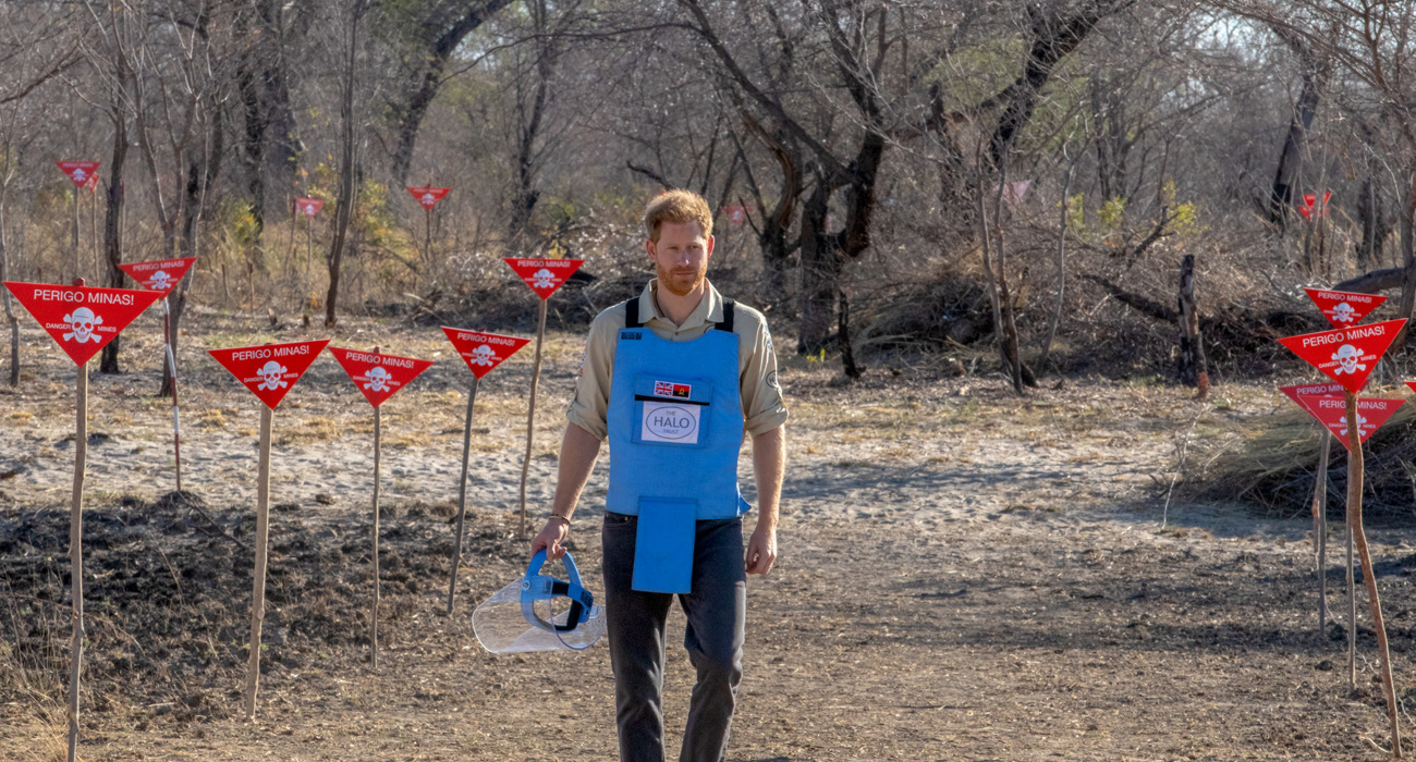 Prince Harry walks through a minefield in Angola, wearing PPE and holding a visor next to red danger signs