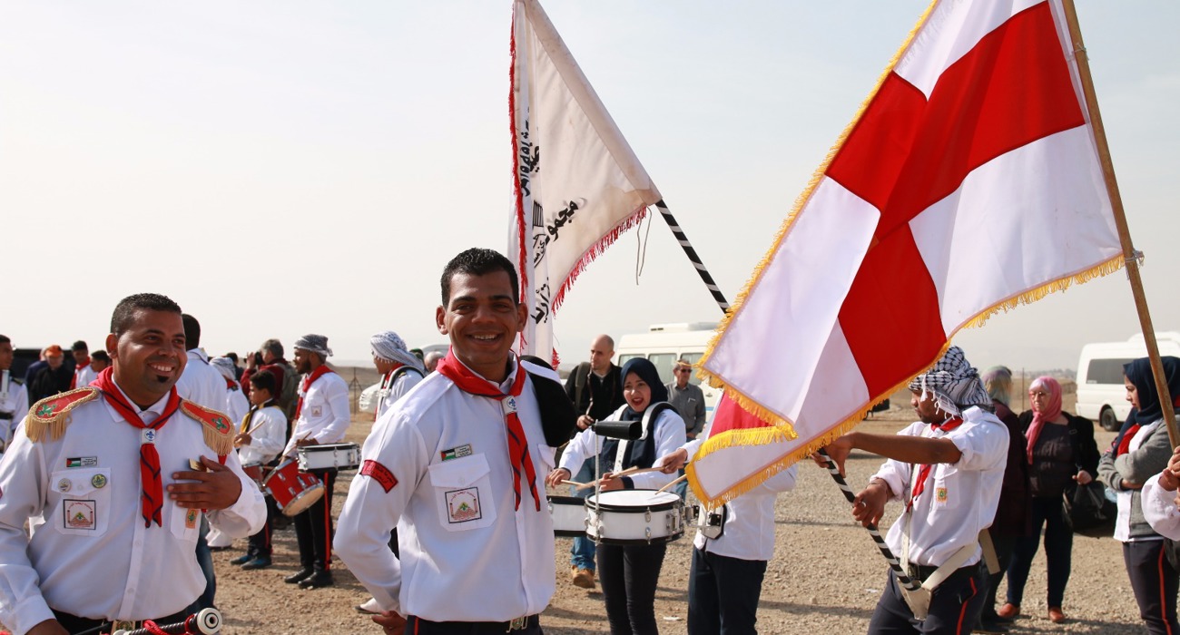 Pilgrims walk through the Baptism Site waving flags and smiling