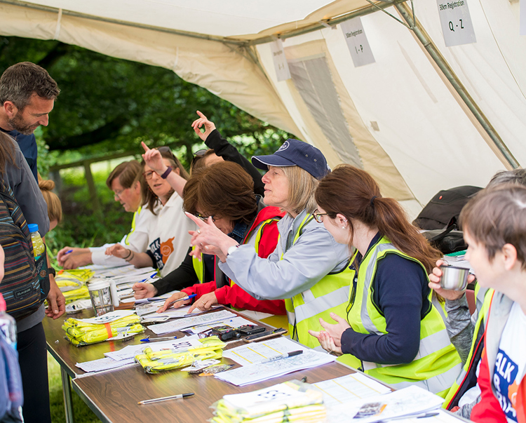 Staff sit behind tables outside as they take registrations for people who will be walking for Syria