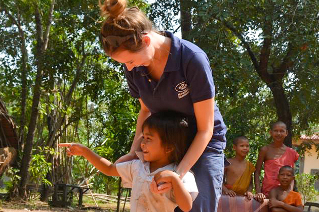 Camilla Thurlow, leans over smiling at a child who is pointing 