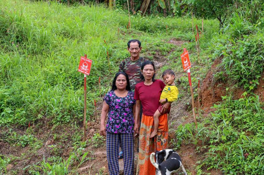 Cheng Seang and his family stand on grassy land marked with mine warning signs