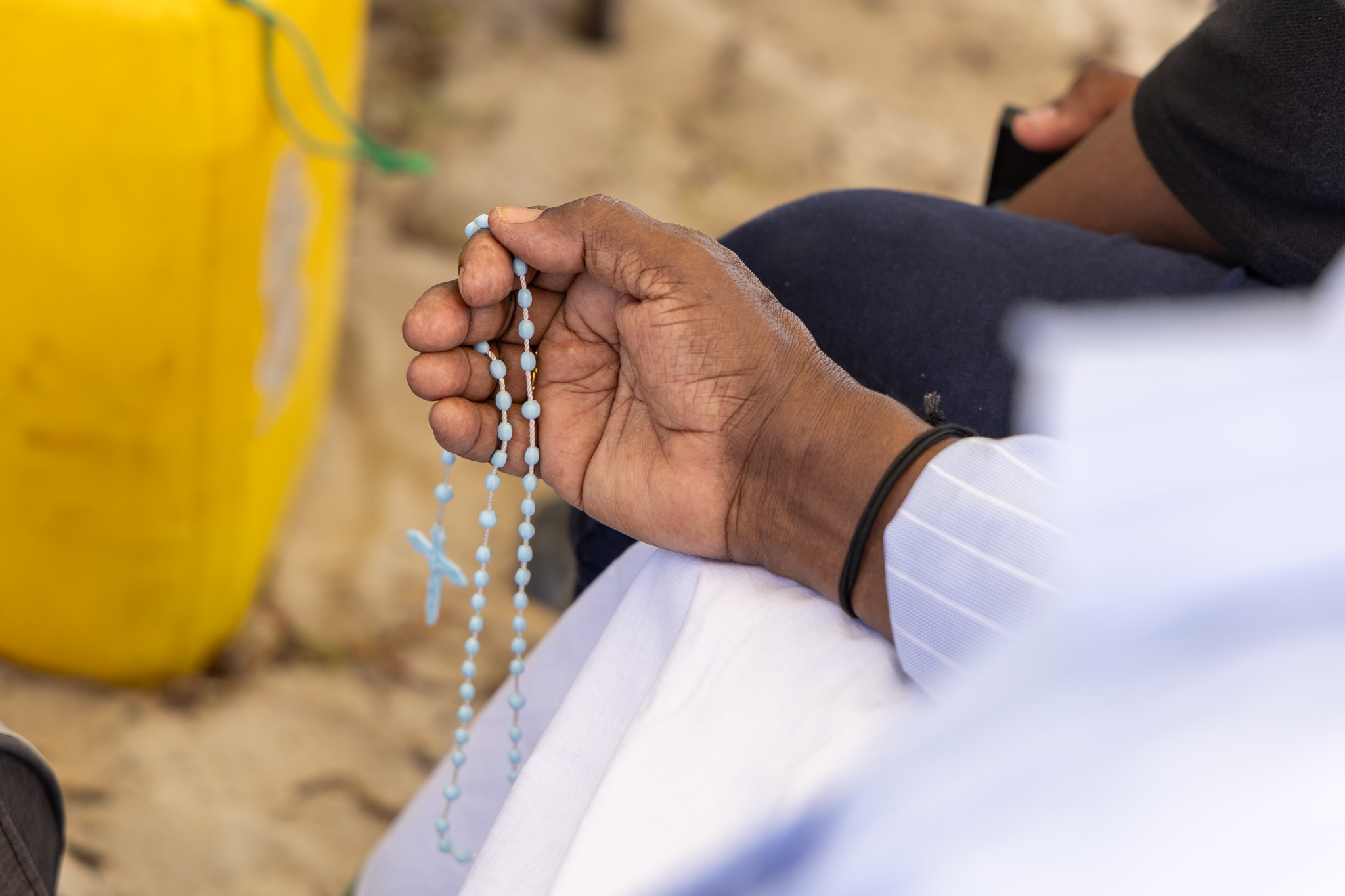 The hand of a church patron holding a light blue rosary. 
