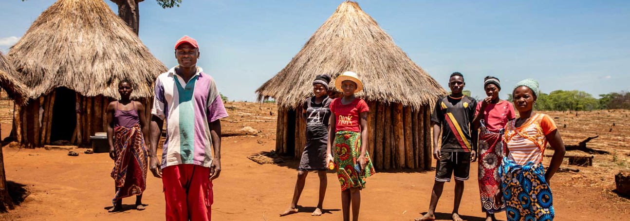 A group of Zimbabwean villagers stand on the ground outside their houses
