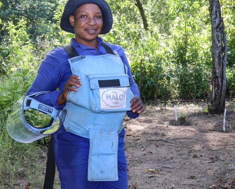 Precious Munetsi, a deminer in Zimbabwe, stands in a minefield in front of trees and bushes