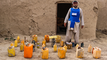 HALO Trust deminer in protective gear, standing next to unearthed improvised explosive devices (IEDs), highlighting the ongoing threat posed by unexploded ordnance