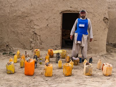 HALO Trust deminer in protective gear, standing next to unearthed improvised explosive devices (IEDs), highlighting the ongoing threat posed by unexploded ordnance