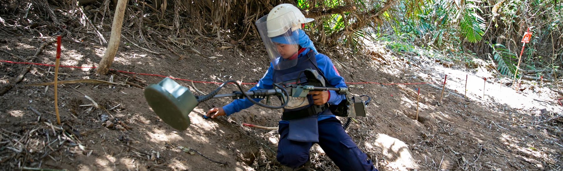 A deminer kneels whilst holding a detector in the jungle in Cambodia