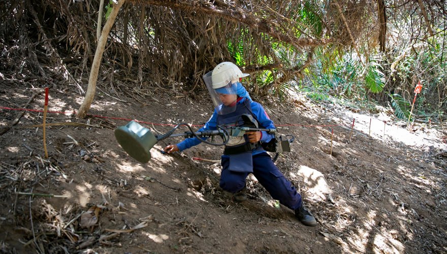 A deminer kneels whilst holding a detector in the jungle in Cambodia