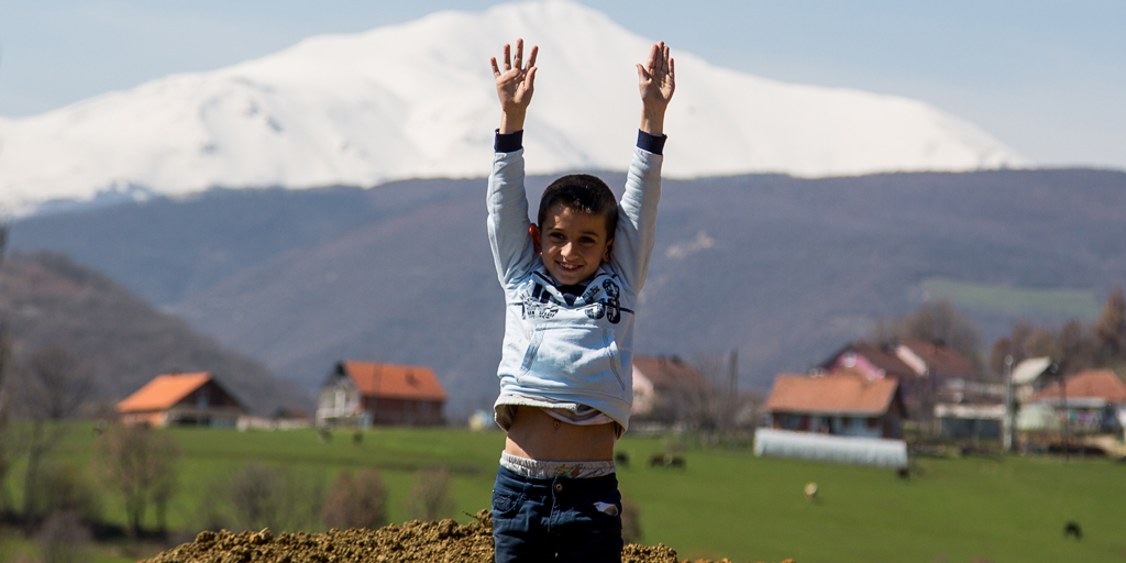 A child smiling in front of houses and a mountain 