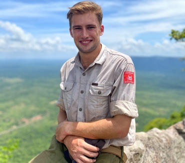 Man smiling, sitting on a rock with a landscape in the background