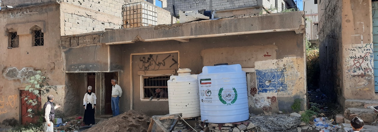Three people stand in front of the rubble of a home in Taiz, Yemen.