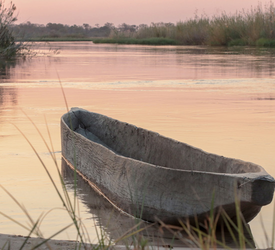 A carved wooden canoe on the Cuito river during sunset